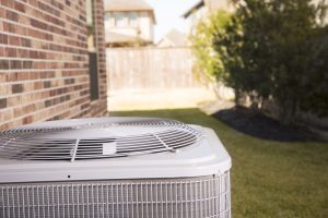 An air conditioner unit outside a brick home in a residential neighborhood. The air conditioner is in a back yard in the hot summer season. Service industry, working class.