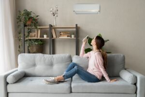 woman-sitting-on-couch-turning-on-ductless-air-handler-with-remote