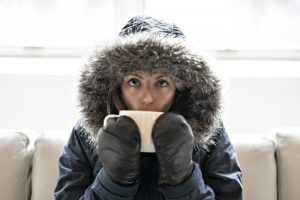 person-indoors-with-coat-and-mittens-on-drinking-hot-tea