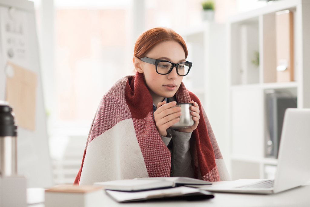 Woman sitting at her desk with a blanket over her shoulders and a cup of coffee