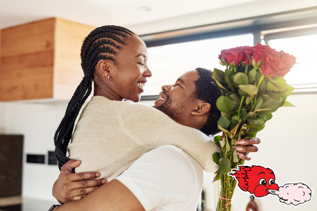 A young man surprising his wife with a bunch of flowers at home